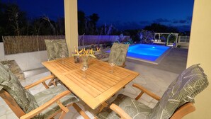 Un patio al aire libre con mesa y sillas de madera, una piscina y una pérgola.
