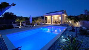 Un área de piscina moderna al aire libre con sillones de descanso y un porche cubierto.