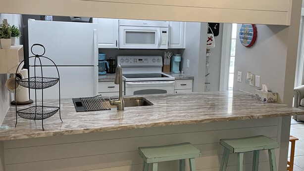 Une cuisine moderne avec des meubles blancs, un four à micro-ondes encastré et un évier. On y trouve deux tabourets vert clair et une petite caisse en bois.