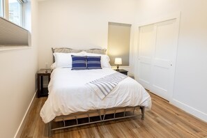 Une chambre à coucher avec un lit, une table de chevet, une lampe et une fenêtre avec des stores.