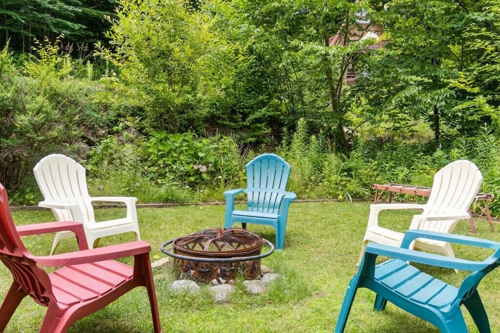 A garden with four Adirondack chairs in red, white, and blue, arranged around a metal fire pit.
