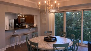 A dining area with a round wooden table and six chairs, a chandelier, and a kitchen with wooden cabinets and a microwave. - Quiet and relaxing with three balconies. Located on the Santa Rosa Sound. (Navarre)