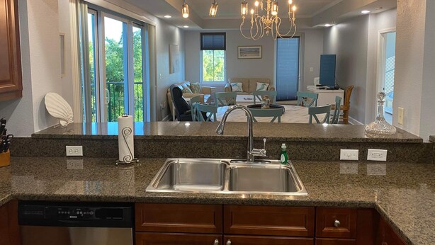 A modern kitchen with granite countertops, stainless steel sink, and wooden cabinets. There is a dining area with a table and chairs, and a chandelier above. - Quiet and relaxing with three balconies. Located on the Santa Rosa Sound. (Navarre)