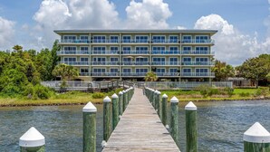 A wooden pier leading to a multi-story hotel with balconies, a view of the water, and greenery around. - Quiet and relaxing with three balconies. Located on the Santa Rosa Sound. (Navarre)