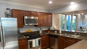 A modern kitchen with stainless steel appliances, wooden cabinets, granite countertops, and a window providing natural light. - Quiet and relaxing with three balconies. Located on the Santa Rosa Sound. (Navarre)