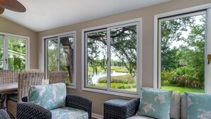 A sunroom with wicker furniture, large windows, and a view of a pond and trees. - 2 BR + Loft/2BA Tarpon Pond Cottage! Great Views! 1 Dog Friendly! (Seabrook Island)
