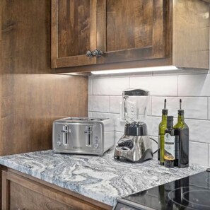 Una cocina con armarios de madera, encimera de mármol, un tostador, una licuadora y dos botellas de aceite de oliva.