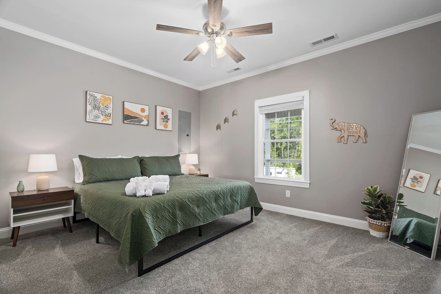 A bedroom with a bed, nightstands, a ceiling fan, artwork, a window, and a mirror.