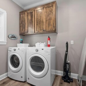 A laundry room with two front-loading washing machines, a fire extinguisher, wooden cabinets, and a vacuum cleaner. - Waterfront Retreat w Dock, Firepit & Boat Access (Belhaven)