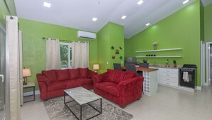 A living room with red sofas, a coffee table, and a kitchen with a stove and sink. - Brand new home in lively West End- Coral Cove (Roatan)