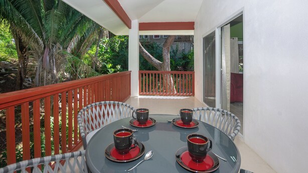 A balcony with a table set for two, two cups of coffee, and a red railing. - Brand new home in lively West End- Coral Cove (Roatan)