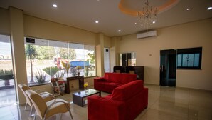 A reception area with a red sofa, beige chairs, a coffee table, and a chandelier. - Hotel Atrium Express (Parauapebas)