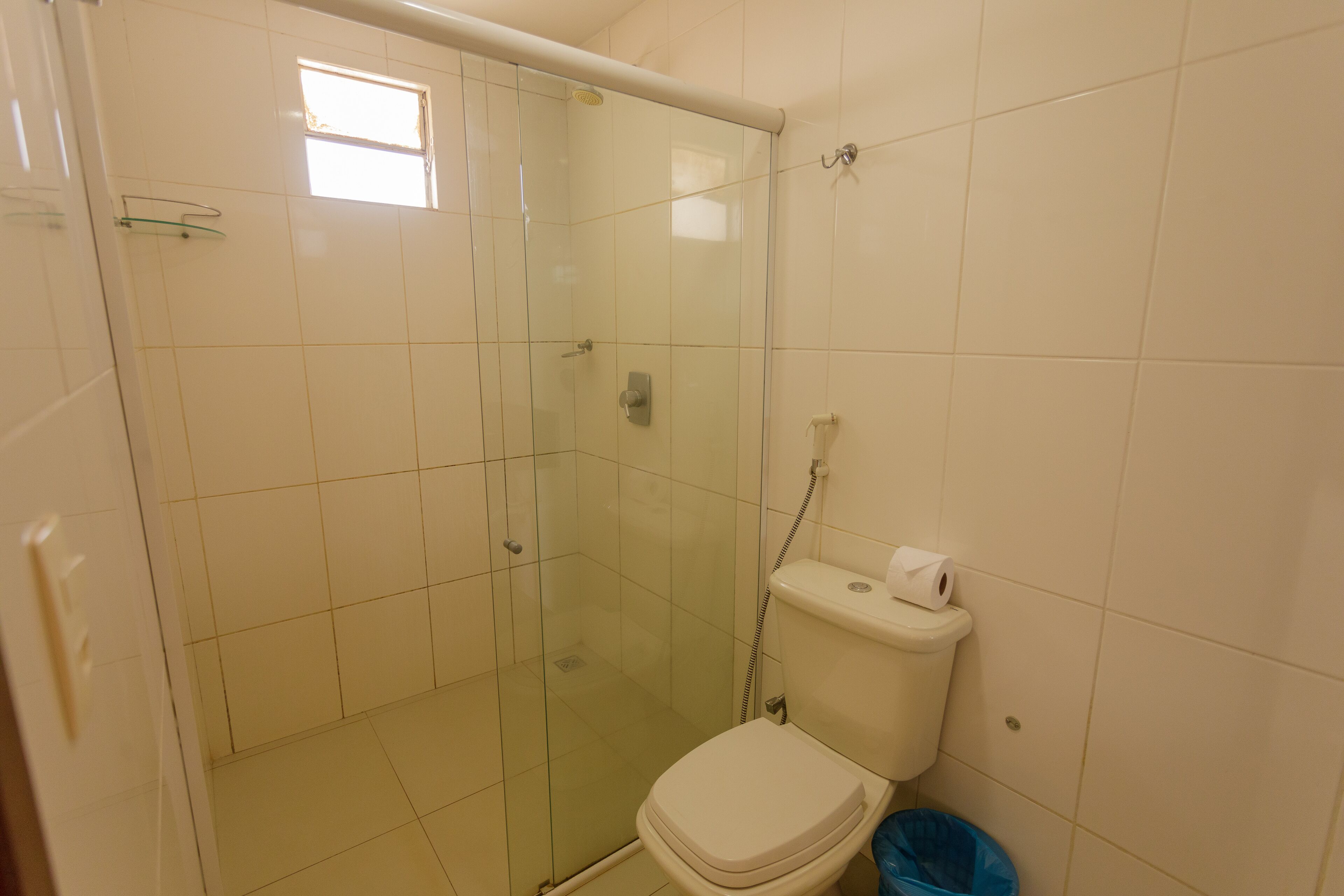 Une salle de bain avec une douche à parois de verre, des toilettes et une poubelle bleue.