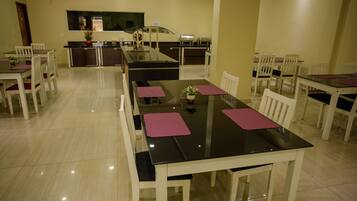 Un comedor con una mesa larga, sillas blancas y una cocina al fondo.