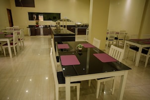 Un comedor con una mesa larga, sillas blancas y una cocina al fondo.