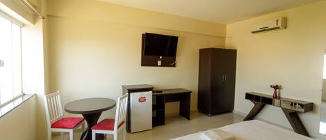A hotel room with a bed, a desk, a chair, a small refrigerator, a television, and a wardrobe.