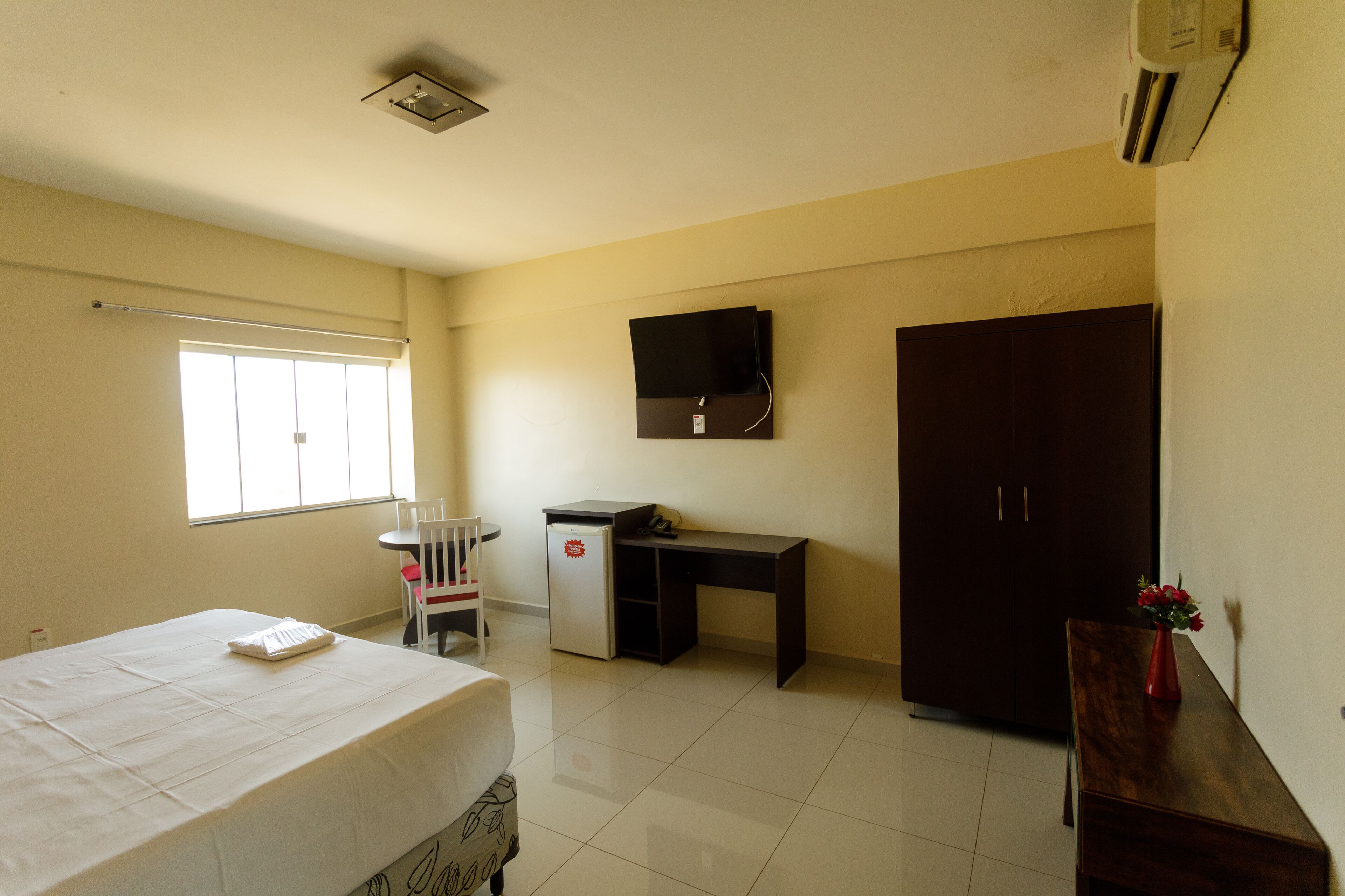 A hotel room with a bed, a desk, a chair, a wardrobe, and a TV mounted on the wall.
