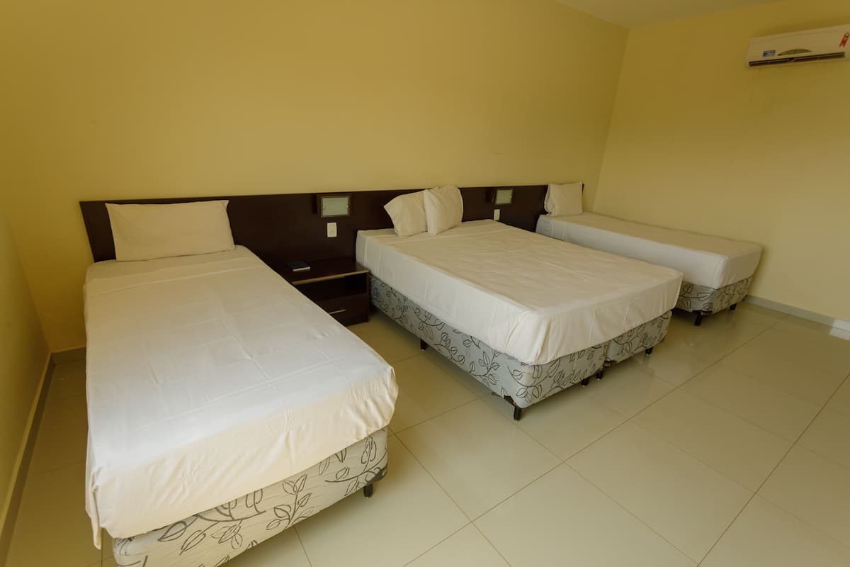 Quarto com três camas de solteiro, cada uma com travesseiro e mesa de cabeceira.