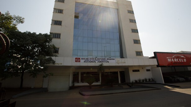 A modern hotel with a large glass facade, a sign indicating availability, and a parking area.