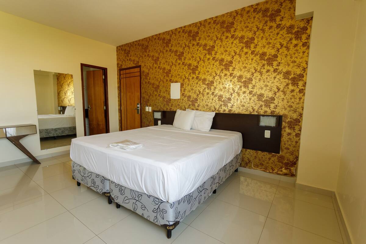 Quarto de hotel com uma cama grande, banheiro com espelho e parede estampada.