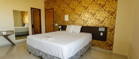 A hotel room with a large bed, a bathroom with a mirror, and a patterned wall.