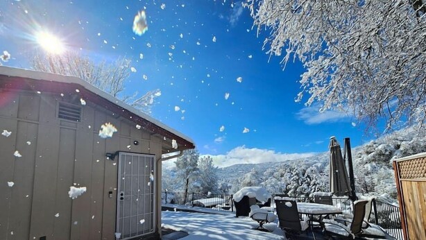 Un espacio al aire libre cubierto de nieve, con un edificio, mesas y sillas.