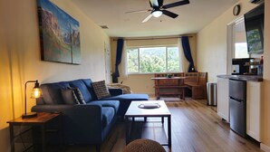 Una sala de estar con sofá, mesa de centro y reposapiés, un comedor con banco, y una cocina con refrigerador y estufa.