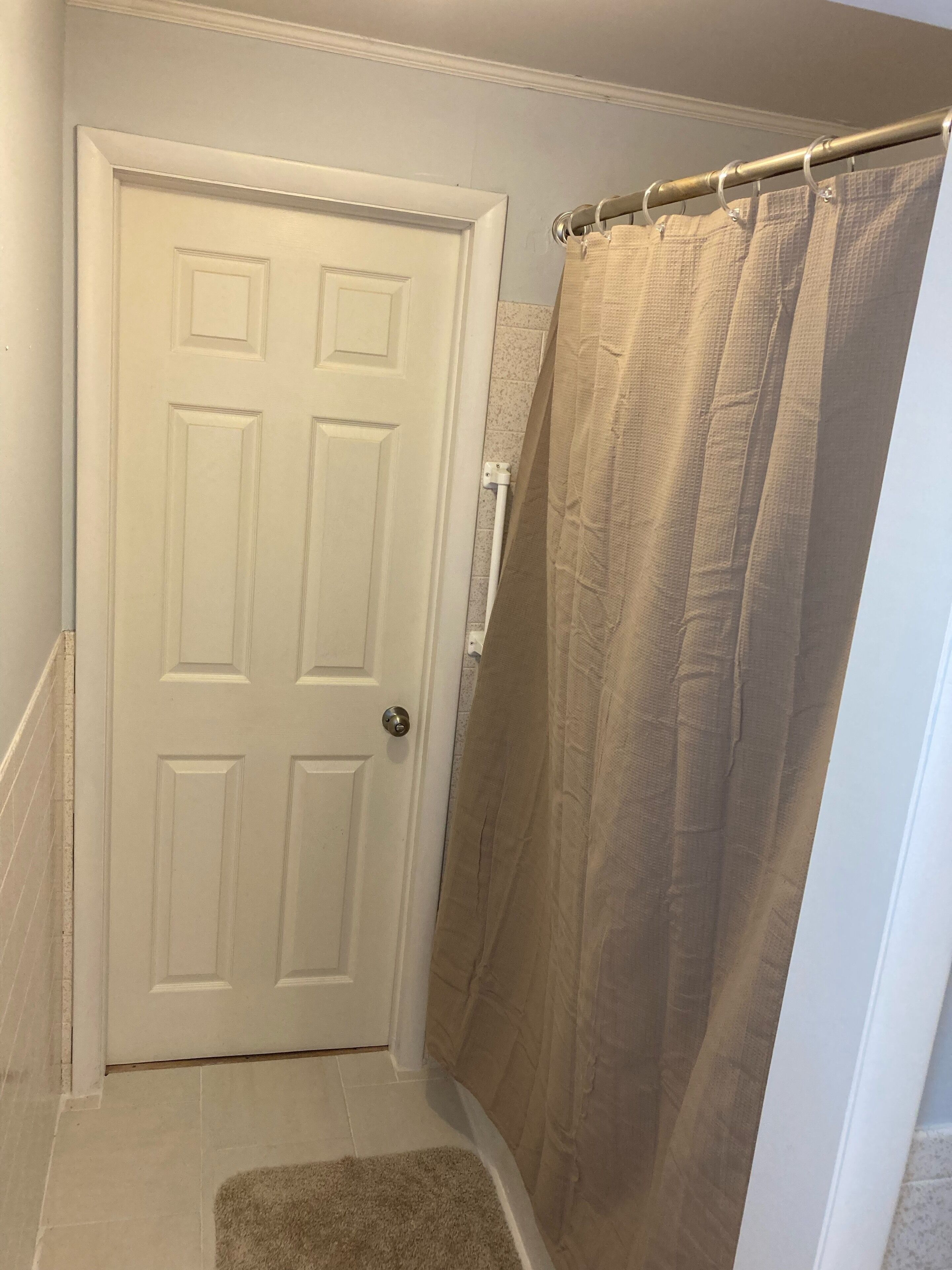 Un baño con una puerta blanca, una cortina de ducha y una alfombra pequeña.