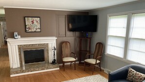A living room with a fireplace, two armchairs, a sofa, a television, and a window with blinds. - Visit Monticello, Wineries, UVA & More (Troy)