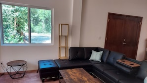 Una sala de estar con un sofá de cuero negro, una mesa de centro de madera, una pequeña mesa redonda y una estantería alta.