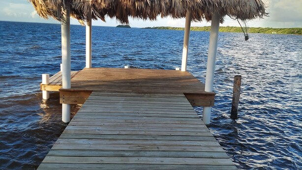 Un muelle de madera que lleva a una construcción de techo de paja sobre el agua.