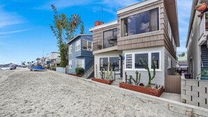 Una proprietà fronte spiaggia caratterizzata da architettura moderna, con una casa a due piani, ampie finestre e un balcone.