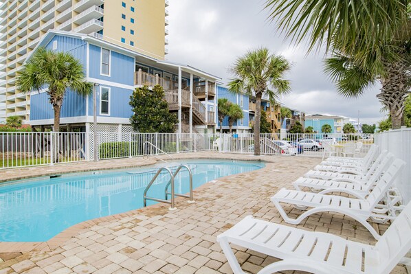 A pool area with white lounge chairs, a pool, and a white fence.