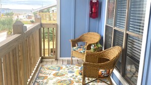 Ein Balkon mit Holzgeländer, einem Korbstuhl und einem bunten Teppich.