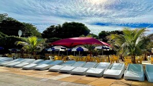 A poolside area with sun loungers and umbrellas, surrounded by palm trees and greenery. - DiRoma Fiori com um dia no Acqua park (Caldas Novas)