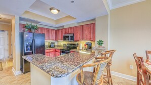 A kitchen with granite countertops, red cabinets, and a central island with bar stools. - New Low Fall/Winter Prices! 2BR2BA Beauty in Gulf Shores Crystal Tower 608 (Gulf Shores)