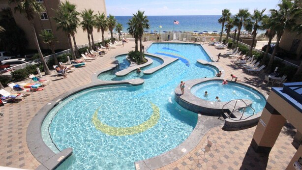 A pool area with multiple swimming sections, lounge chairs, and palm trees. - New Low Fall/Winter Prices! 2BR2BA Beauty in Gulf Shores Crystal Tower 608 (Gulf Shores)