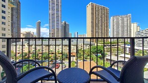 A balcony with wicker chairs, overlooking a cityscape with high-rise buildings and a parking area.