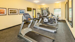 Un gimnasio con cintas de correr, máquinas de pesas y colchonetas de ejercicio.