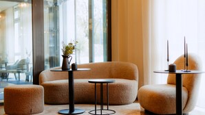 A modern lounge area with a sofa, two small tables, and a coffee table, all in a neutral color scheme. - Moods Hotel Dortmund (Dortmund)