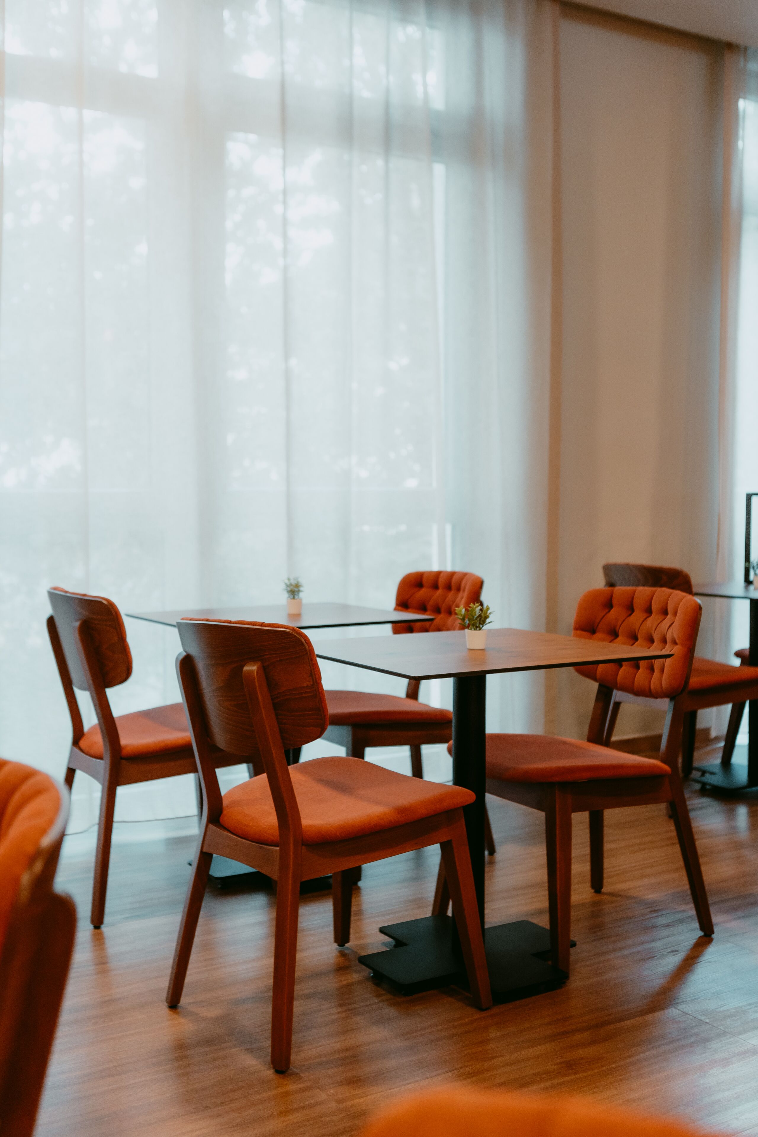 Comedor con mesa de vidrio rodeada de sillas de madera con cojines naranja.