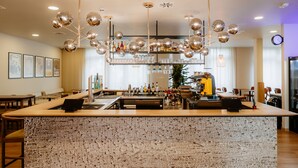 A bar area with a central island, bar stools, a cash register, and a variety of bottles and glasses. - Moods Hotel Dortmund (Dortmund)