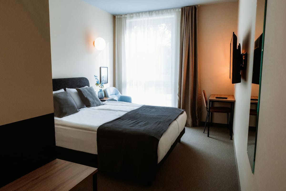 Une chambre d’hôtel équipée d’un lit, d’une table de chevet, d’un bureau, d’une chaise et d’un téléviseur fixé au mur.