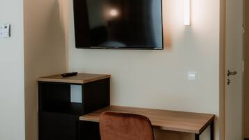 Una habitación con una televisión de pantalla plana montada en la pared, un escritorio de madera, un armario negro y una silla marrón.