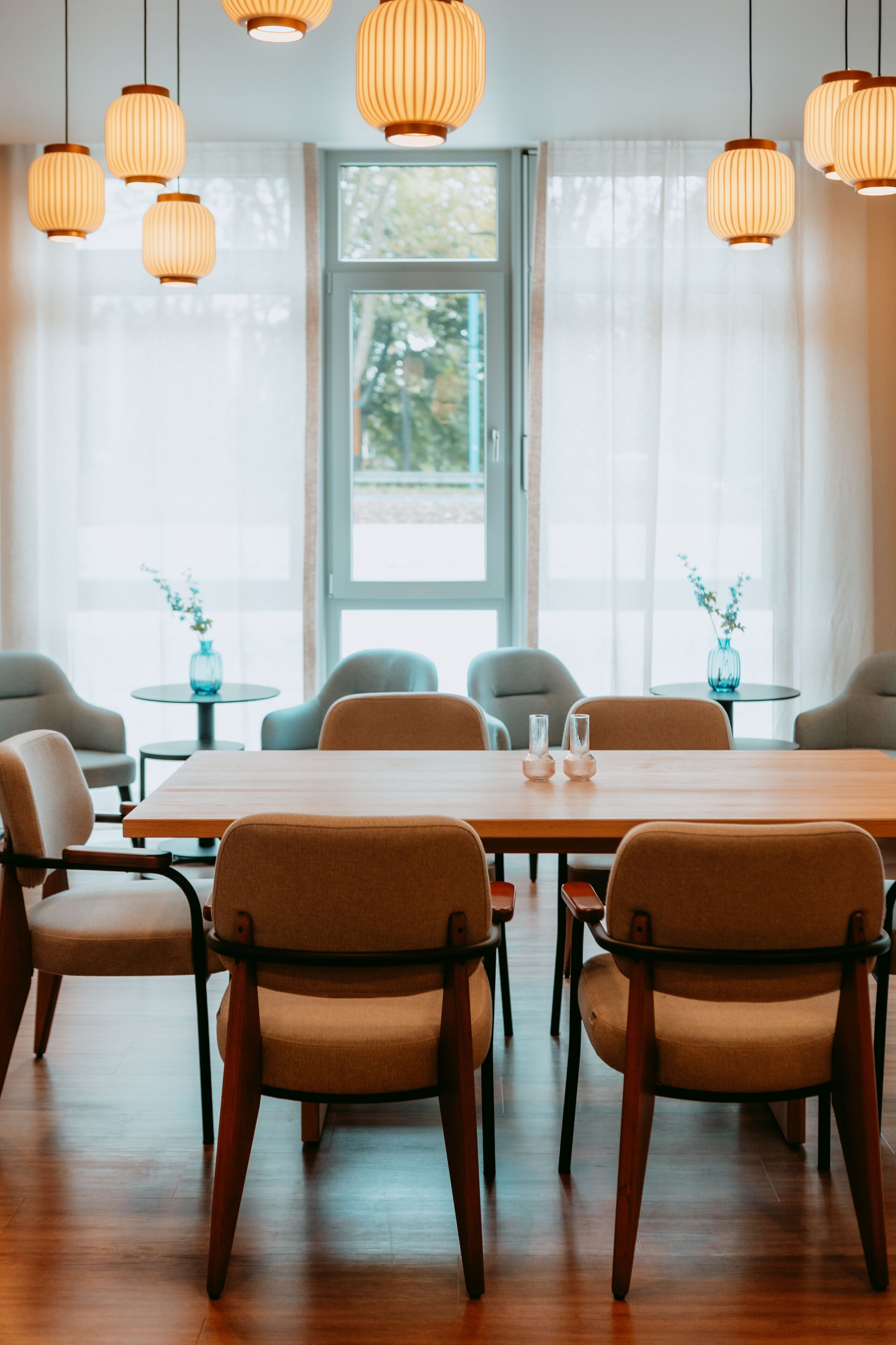 A dining area with a wooden table and chairs, a window with curtains, and hanging pendant lights.