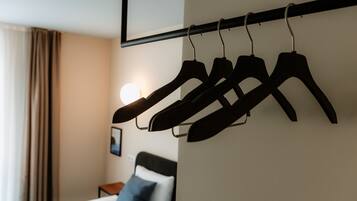 A hotel room with a bed, a bedside table, and a wall-mounted rack holding several black hangers.