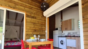 Ein gemütliches Blockhaus mit Holzvertäfelung, einem Essbereich mit roten Stühlen, einem Bett mit Baldachin und einer Küche mit modernen Geräten.