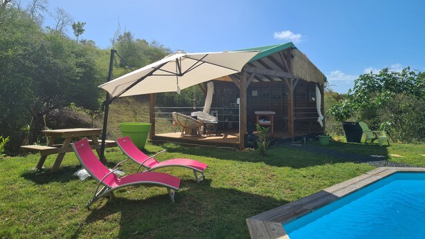 Eine Holzhütte mit überdachter Terrasse, Pool und rosa Liegestühlen.