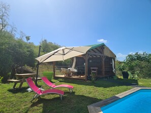 Une cabane en bois dotée d’un patio couvert, d’une piscine et de chaises longues roses.