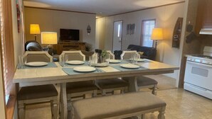 Een eetruimte met een lange tafel gedekt voor vier personen, banken en een keuken op de achtergrond.